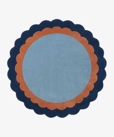 Top-down view of the circular Azure Halo rug featuring a light blue center framed by a double scalloped border in warm terracotta and deep navy blue.