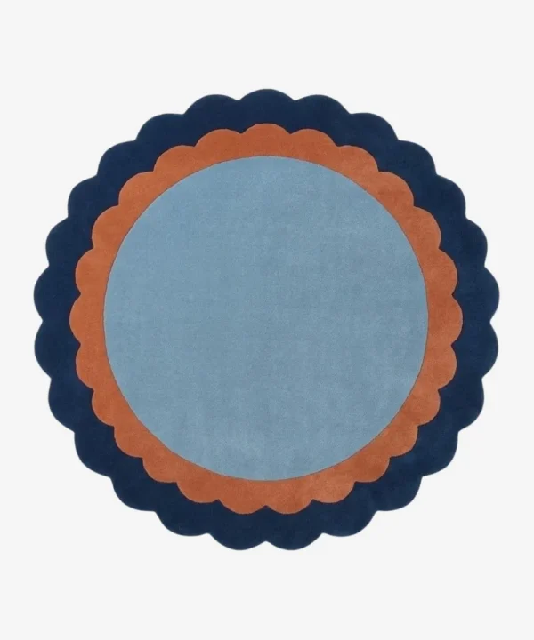 Top-down view of the circular Azure Halo rug featuring a light blue center framed by a double scalloped border in warm terracotta and deep navy blue.
