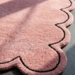 Close-up detail of the Blush Halo rug in sunlight, highlighting the dense, plush hand-tufted pink wool pile and the crisp, deeply carved thin black line that accents the scalloped border.