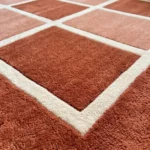 Close-up, angled view of the Canyon Panel rug, highlighting the dense hand-tufted wool texture, the crisp cream grid lines, and the contrasting plush rust and peach square blocks.