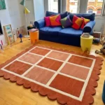 Perspective view of the Canyon Panel scalloped rug styled in a bright, eclectic living room, adding a warm geometric focal point on a hardwood floor in front of a blue sofa.