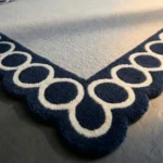 Close-up detail of the Chain Frame rug's corner, highlighting the dense, plush hand-tufted wool pile and the crisp definition of the white-on-navy interlocking circle pattern.