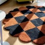 Close-up detail of the Cinder Form round rug, highlighting the dense, hand-tufted wool pile, the crisp carved definition between the cream and charcoal grey sections, and the thick, plush texture in natural sunlight.