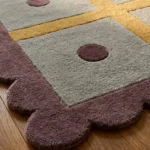 Close-up angled detail of the Honey Lattice runner rug on a wooden floor, highlighting the plush hand-tufted wool texture of the grey base, the yellow grid lines, the purple dot, and the deeply carved purple scalloped border.