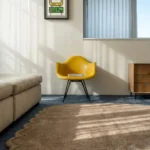 A wider perspective view of the Latte Halo rug bathed in natural sunlight, highlighting its thick hand-tufted wool pile and elegant wavy silhouette within a contemporary room setting.