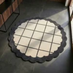 Perspective view of the round Orbital Grid rug styled on a dark grey tile floor, showcasing the striking contrast between its geometric grid center and playful wavy border in a sunlit entryway.