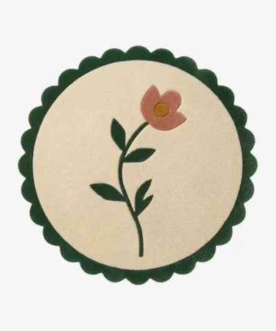 Top-down view of the circular Petal Poise rug, featuring a soft cream background adorned with a stylized pink flower and green stem, perfectly framed by a thick forest green scalloped border.