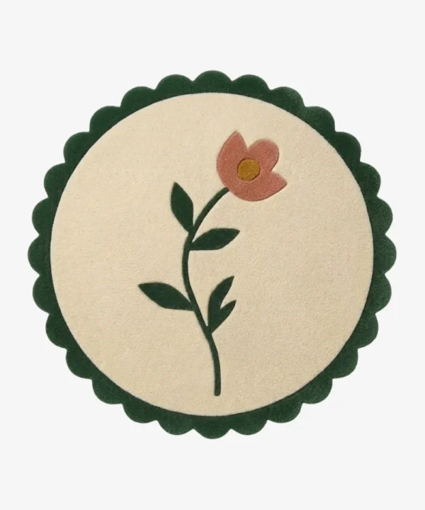Top-down view of the circular Petal Poise rug, featuring a soft cream background adorned with a stylized pink flower and green stem, perfectly framed by a thick forest green scalloped border.