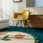 Close-up angled view of the Petal Poise rug bathed in natural sunlight, highlighting the thick hand-tufted wool cut pile, the textured pink flower motif, and the plush green scalloped edge.