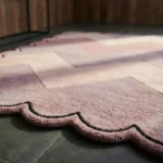 Close-up detail of the Rose Chevron rug bathed in sunlight, highlighting the thick hand-tufted wool pile, the crisp color transitions of the zigzag pattern, and the sharp black line defining the scalloped edge.