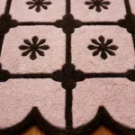 Close-up detail of the Roselle Lattice rug, showcasing the plush hand-tufted pink wool pile, the crisp dark brown floral motif, and the intricately carved brown scalloped edge.