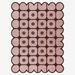 Top-down view of the rectangular Roselle Lattice rug, featuring a soft pink base with a dark brown grid pattern, a central floral motif in each square, and a matching continuous brown scalloped border.