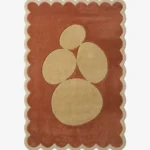 Top-down view of the rectangular Sienna Forms rug, featuring an abstract cluster of organic cream pebble shapes set against a warm rust orange field and framed by a matching cream scalloped border.