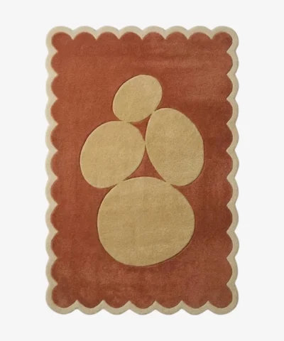Top-down view of the rectangular Sienna Forms rug, featuring an abstract cluster of organic cream pebble shapes set against a warm rust orange field and framed by a matching cream scalloped border.