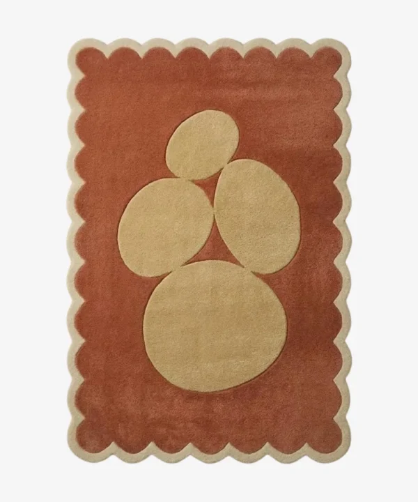 Top-down view of the rectangular Sienna Forms rug, featuring an abstract cluster of organic cream pebble shapes set against a warm rust orange field and framed by a matching cream scalloped border.