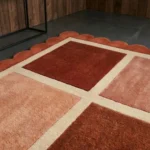 Close-up detail of the Sunset Panel rug bathed in sunlight, highlighting the dense hand-tufted wool pile and the crisp cream grid lines separating the plush rust and peach squares.