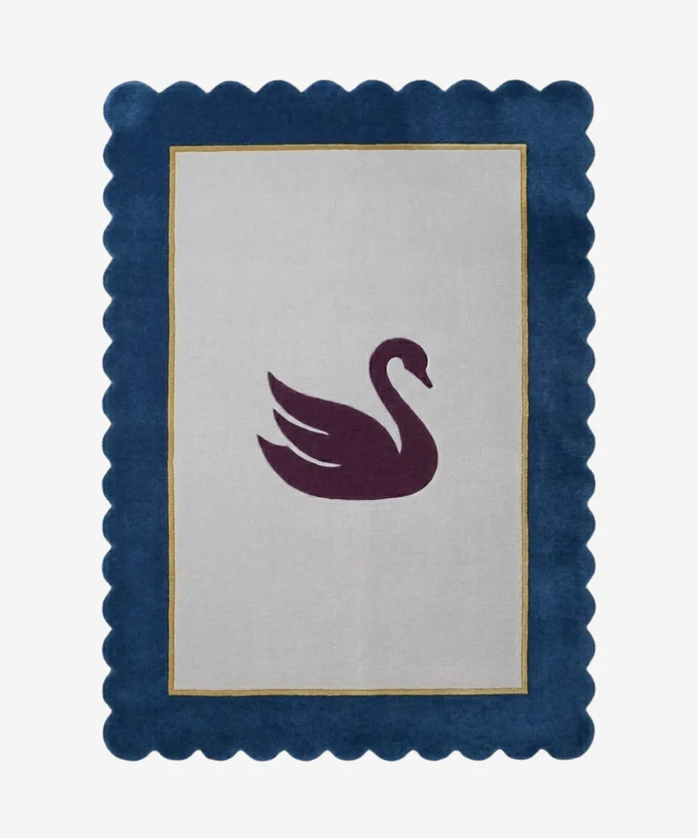 Top-down view of the Swan Crest hand-tufted wool rug featuring a central dark purple swan silhouette on a light grey rectangular field, framed by a thin gold line and a bold navy blue scalloped border.