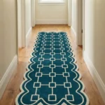 Long teal and cream Terenza Coil Runner Rug with scalloped borders laid out on a light wooden floor inside a bright home corridor.