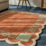Close-up angled view of the Terrain Frame rug basking in sunlight, highlighting the thick hand-tufted wool pile, the crisply carved sage green geometric corner detailing, and the plush cream scalloped border.