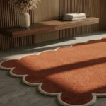 Angled close-up of the solid rust orange Terryn Vale Wool Rug highlighting the thick hand-tufted cut pile construction and cream scalloped edge binding.