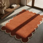 Terryn Vale Hand Tufted Wool Rug in burnt orange with scalloped edges placed on a grey concrete floor in a modern sunlit room with slatted wooden wall accents.