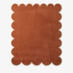 Overhead view of the hand-tufted Terryn Vale Wool Rug displaying a solid rust orange center with dense cut pile and a contrasting cream scalloped border.