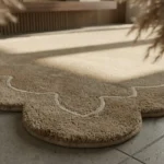 Close-up angled detail of the Velune Nest rug basking in sunlight, highlighting the thick hand-tufted tan wool pile and the crisply carved cream contour line.