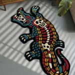 Top-down flat perspective of the die-cut Alligator Skeleton traditional tattoo rug, featuring a crisp white gator bone structure on a solid black base, resting on a smooth grey concrete floor bathed in natural sunlight.