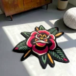 Perspective view of the rectangular American Traditional Rose Rug, featuring a traditional tattoo flash-style repeating pattern of two red roses and stars on a cream background with a scalloped black border, styled on a modern concrete floor next to a textured white pouf and a mid-century wooden cabinet bathed in natural sunlight.