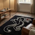 Extreme close-up of the Black Panther Tattoo Rug's face detail in bright natural sunlight, emphasizing the dense, plush hand-tufted wool texture and the precision of the carved lines defining the yellow eyes, red nose, and sharp white teeth.