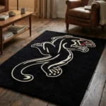 Angled close-up of the front half of the Black Panther Tattoo Rug on a concrete floor, highlighting the traditional tattoo flash artistry of the crouching black panther's face with its fierce yellow eyes and red mouth.