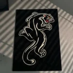 Top-down flat view of the die-cut Black Panther Tattoo Rug, resting on a grey concrete floor, showcasing its irregular shape, crouching panther silhouette, and vibrant red, yellow, and blue traditional tattoo-style face and border accents.
