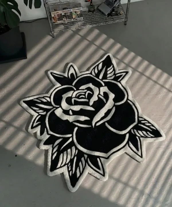 Top-down view of the Black Veil rose-shaped rug resting on a concrete floor with striking window blind shadows cast across its surface, emphasizing the bold contrast of the white carved lines on the black wool background.