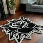 Perspective view of the Black Veil black and white traditional tattoo rose rug styled on a wooden floor in a living room next to a classic black fireplace, a potted plant, and a light grey leather sofa.