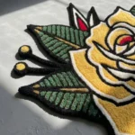 Close-up angled detail of the edge of the Classic Inked Rose rug, showcasing the plush thickness of the hand-tufted pile and the clean, carved lines defining the stylized green leaves.