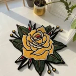 Perspective view of the die-cut Classic Inked Rose traditional tattoo rug styled on a warm hardwood floor in a cozy living space, positioned near a classic leather armchair.