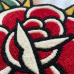 Close-up angled detail of the Classic Rose Tattoo Rug, showcasing the plush green hand-tufted wool leaves and deep carving against the dark hardwood floor.