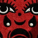 Close-up angled detail of the Crying Heart rug, showcasing the plush velvet-like texture and crisp carved details of the mouth and sharp white teeth against the red wool.