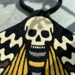 Close-up detail of the hand-tufted Death Head Moth rug, focusing on the textured wool pile of the central skull motif and the top antennae.