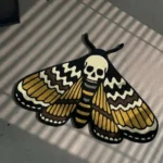 Angled perspective view of the traditional tattoo style Death Head Moth rug styled in a modern room, lying on a concrete floor next to a black wireframe chair.