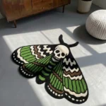 High-angle view of the Death Moth neo-traditional tattoo flash rug resting on a smooth grey concrete floor next to a white pouf, with dramatic window shadows cast across its skull and wing details.