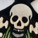 Close-up macro detail of the Death Moth rug, highlighting the dense hand-tufted 100% New Zealand wool pile and the crisp 3D carving of the stark white skull against the black and green background.