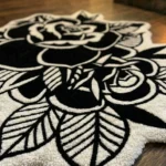 Macro detail of the Dual Rose rug resting on a wooden floor, highlighting the thick, dense hand-tufted wool texture and the deeply carved white leaves against the solid black background.