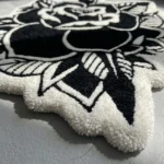 Low-angle close-up view of the Dual Rose rug's corner on a light concrete floor, emphasizing the plush thickness of the hand-tufted wool pile and the intricately carved outer border.