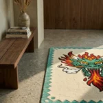Angled perspective view of the Firebreath Dragon Head rug bathed in sharp natural sunlight and shadows, placed on a modern terrazzo floor beside a warm wooden bench and a stack of design books.