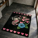 Wide perspective view of the Inkheart Panther tattoo flash rug resting on a dark tile floor in a sunlit modern room, showcasing its rectangular shape bordered by pink hearts at the top and bottom.