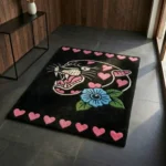 Perspective view of the rectangular black Inkheart Panther rug styled on a dark slate tile floor in a modern entryway, bathed in bright natural sunlight next to a dark wood console table.