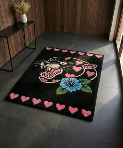 Perspective view of the rectangular black Inkheart Panther rug styled on a dark slate tile floor in a modern entryway, bathed in bright natural sunlight next to a dark wood console table.