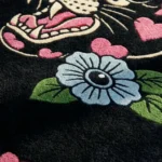 Extreme close-up macro detail of the Inkheart Panther rug, highlighting the dense hand-tufted wool pile, the deeply carved blue flower, and the crisp 3D detailing of the panther's fierce teeth and pink mouth.