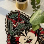 Angled perspective view of the hand-tufted Lady Face tattoo rug bathed in natural sunlight on a white painted floor, styled next to a vibrant green potted plant in a gold pot.